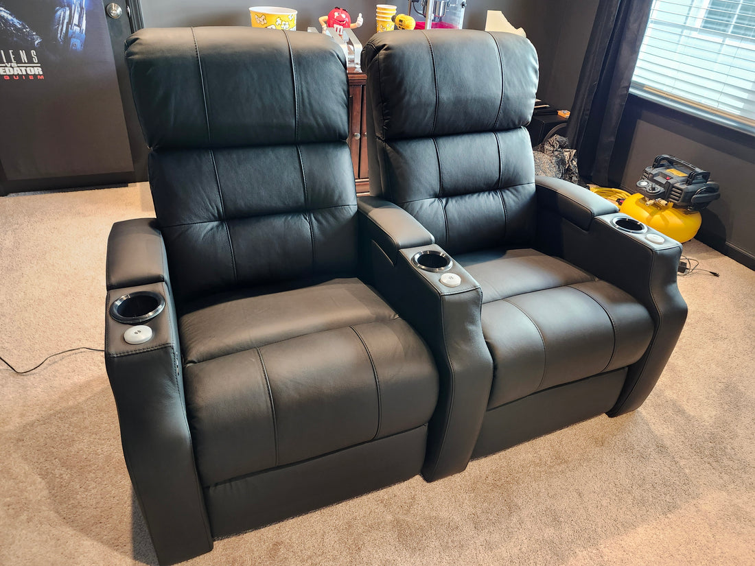 Two black leather home theater recliners with center console and built-in cup holders on carpeted floor
