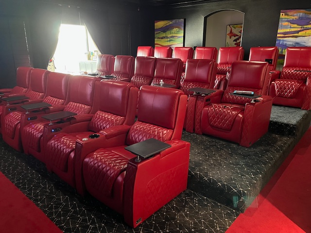 Red leather home theater recliners arranged in multiple rows with cup holders and tray tables in a dedicated media room